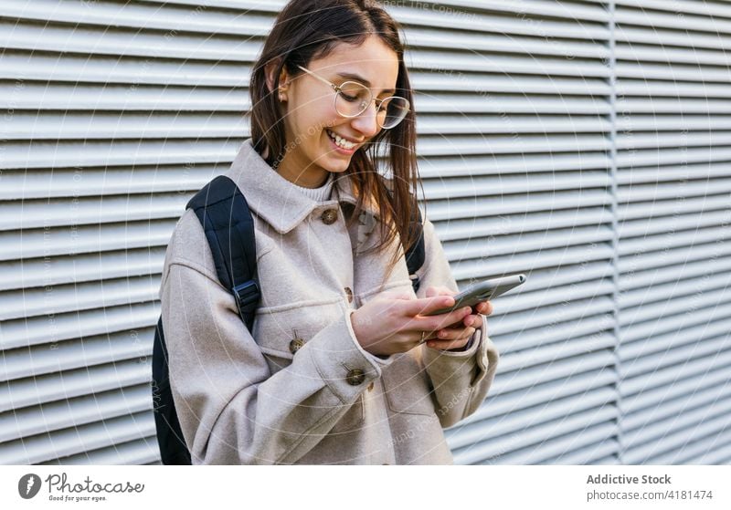 Crop happy woman using smartphone on street browsing toothy smile sidewalk surfing cellphone device carefree content gadget backpack beautiful free time