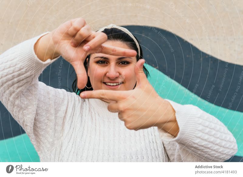 Glad woman showing photo gesture near wall outdoors frame smile perspective arms raised friendly portrait photography plump enjoy content white knitwear