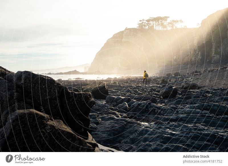 Unrecognizable traveler walking on rocky seashore surrounded by sharp cliffs seacoast rough severe stiff highland geology mountain stone formation terrain