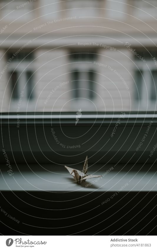 Crane origami on windowsill at home in evening crane handmade handicraft creative design paper house twilight similar facade building domestic solitude silent