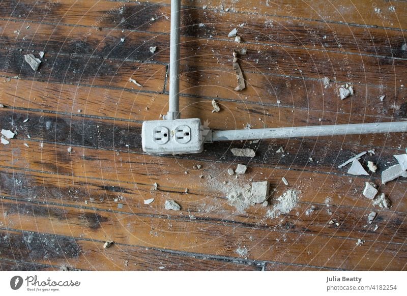 Abandoned outlet laying on old wood floors at construction site; drywall scraps and dirt surrounding it wooden metal rusty antique texture electric electrical