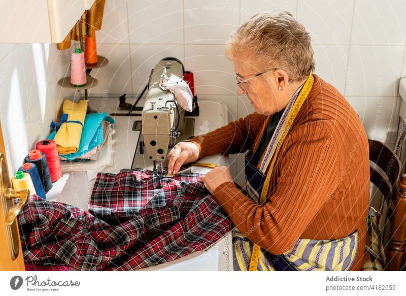 Focused elderly dressmaker sewing clothes in workshop woman seamstress thread stitch sewer senior craftswoman female sewing machine artisan creative tool