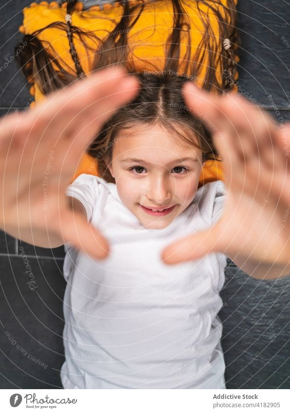 Adorable girl lying on floor and raising hands towards camera hand raised content cute positive glad childhood playful sweet optimist pillow happy braid