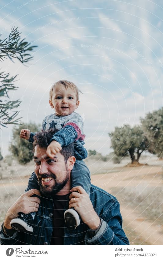 Man with cute child on shoulders in nature father ride cheerful care together boy son countryside weekend kid fatherhood joy childhood little glad parent