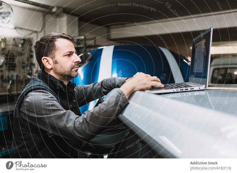 Attentive male mechanic typing on laptop in garage screen attentive internet man auto workshop using gadget device netbook watching master transport concentrate