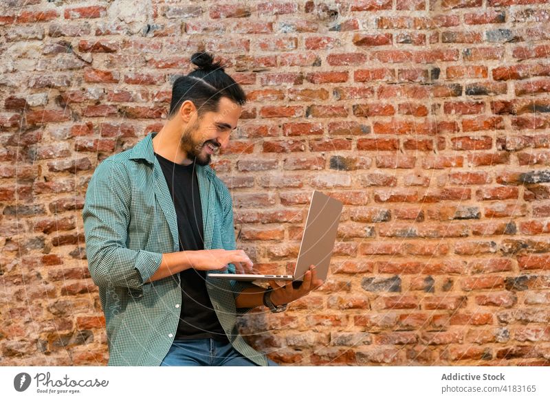 Smiling barista using laptop in cafe man work browsing hipster cheerful bartender loft male netbook gadget device shabby brick wall style surfing internet young