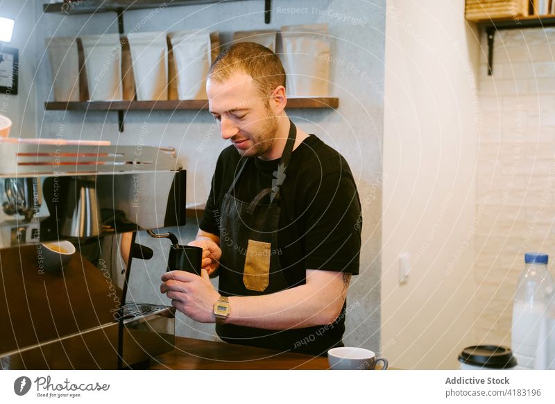 Content barista preparing coffee in coffee machine coffeemaker milk whip man prepare drink cafe male coffee shop cafeteria pitcher jug staff employee service