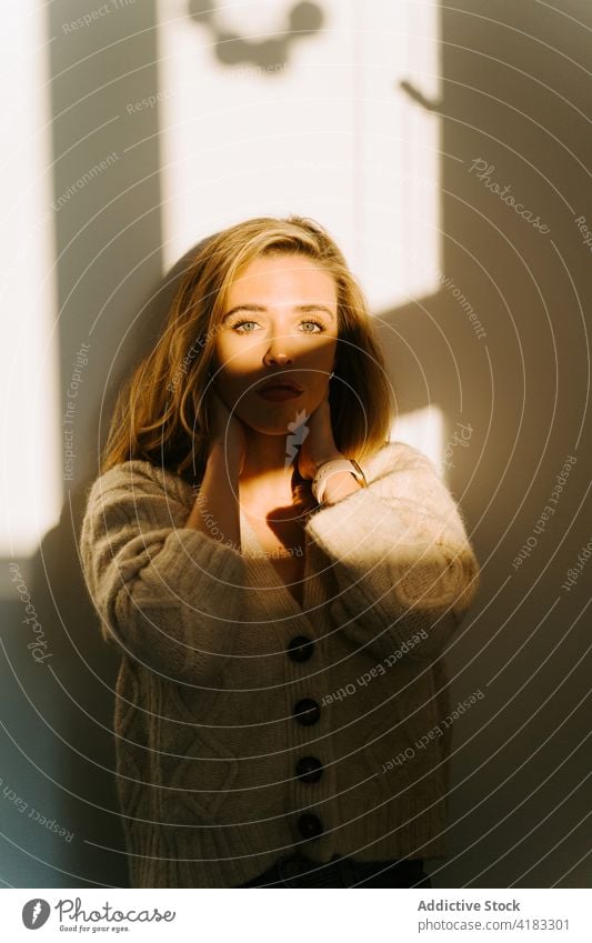 Tender woman in room lit by sunlight tender charming tranquil cozy delicate appearance beauty female home calm knitted cardigan wall young style relax comfort