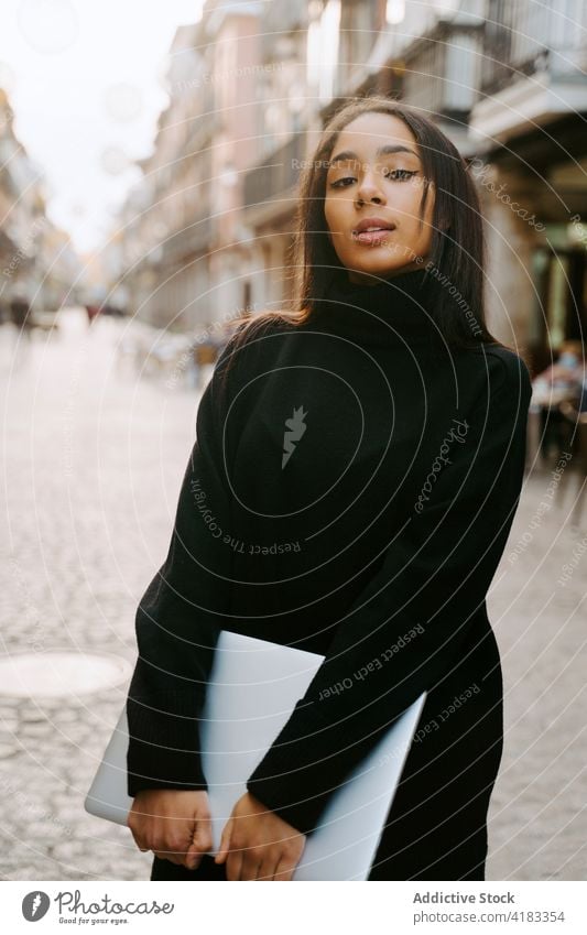 Cheerful woman with laptop on sunny street cheerful urban student pedestrian town excited netbook portable sunlight style device smile contemporary ethnic