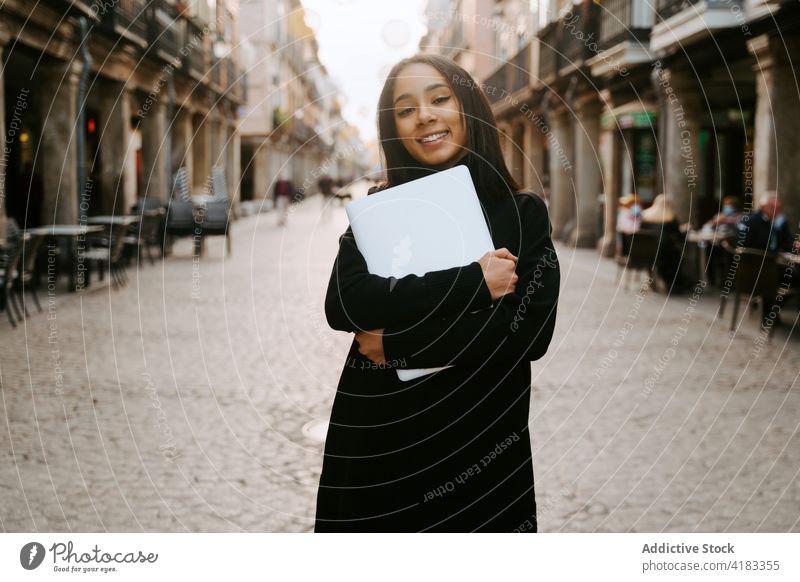 Cheerful woman with laptop on sunny street cheerful urban student pedestrian town excited netbook portable sunlight style device smile contemporary ethnic