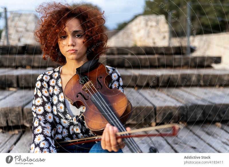 Attractive woman playing violin sitting on boardwalk musician instrument park calm serene talent perform melody skill acoustic attractive sound song hobby