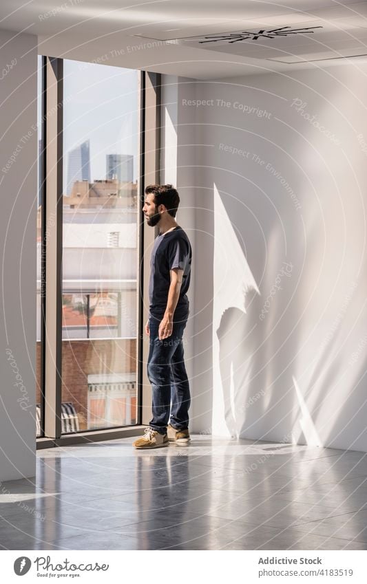 Man standing near window in spacious office hall man empty facility shadow sunlight geometry male interior shape hallway white wall modern design minimal line