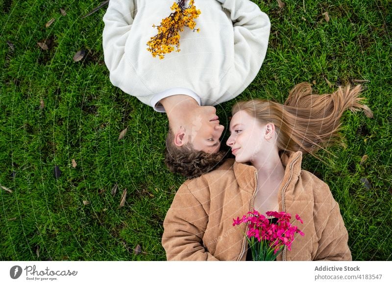 Couple with blossoming flowers lying close on meadow couple relax lawn relationship love gentle spend time summer idyllic rest spare time bright bouquet flora