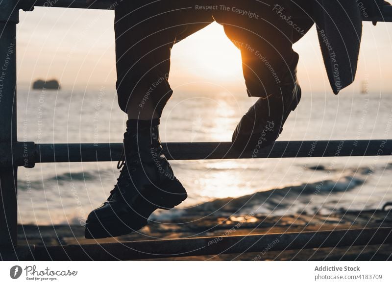 Unrecognizable traveler resting near sea at sunset leg fence ocean wave sundown sunlight relax evening person seaside autumn nature coast shore journey