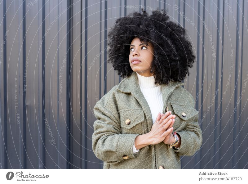 Trendy young black lady standing on street and looking away dreamily woman pensive dreamy pray gesture trendy street style appearance charismatic individuality