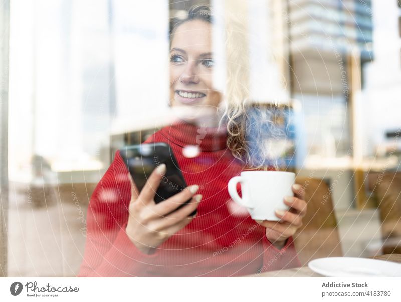 Smiling woman with smartphone and cup of drink in cafe enjoy cheerful browsing beverage carefree internet female hot table sit hot drink mobile coffee tea smile