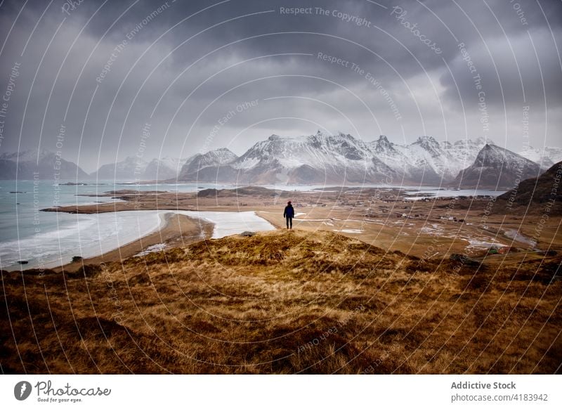 Traveler standing on hill in mountainous area in winter travel frozen sea highland snow admire viewpoint observe norway dry water explorer cloudy cold sky ridge