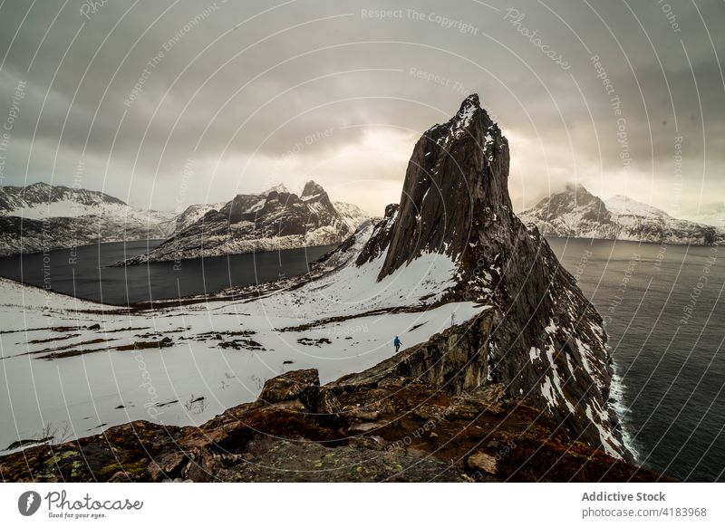 Hiker walking along snowy mountain near sea hike winter traveler explore highland wintertime rocky edge norway landscape tourism wanderlust nature water