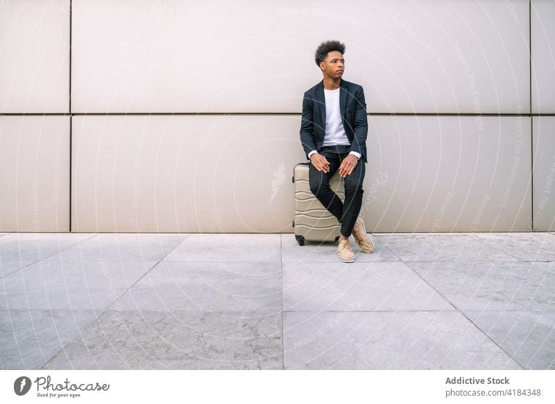 Ethnic man sitting on suitcase near airport building traveler wait luggage tourist peaceful departure male ethnic black african american trip passenger tourism