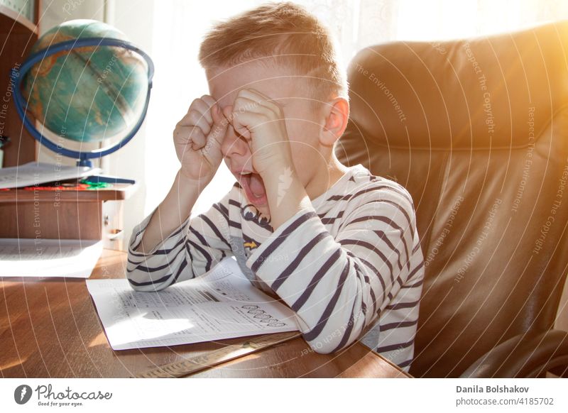 school-age boy crying and screaming while doing homework. the concept of heavy pressure education child student angry stress reading elementary young people kid