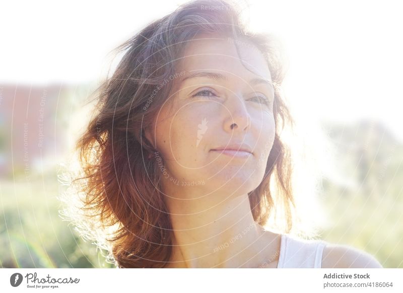 Smiling adult woman resting in meadow on sunny day relax bloom countryside enjoy idyllic glad nature harmony summer human face female wavy hair smile field