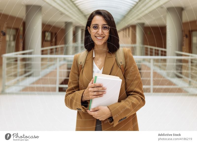 Smiling woman with books in university hall student hallway academic education smile young knowledge female ethnic backpack pile literature study positive