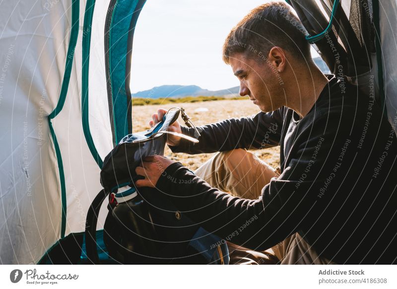 Young pensive camper relaxing in tent in sunny morning man rest backpack dreamy traveler mountain admire trip journey recreation wanderlust male young casual