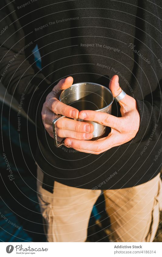 Stylish young guy enjoying hot drink during camping in mountainous countryside man beverage tent recreation hiker confident style nature grassland male trendy