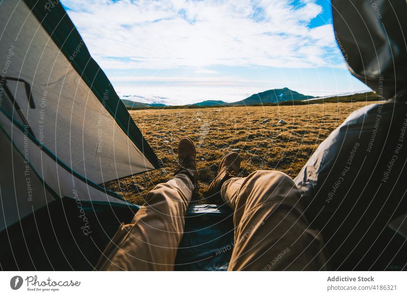 Anonymous male camper recreating in tent during hiking trip in highland man lying mountain nature hill hike traveler recreation relax landscape tourism casual