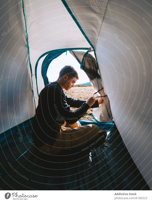 Young stylish guy sitting in tent during camping man camper concentrate rest hike trip alone nature activity hobby male young casual journey travel vacation