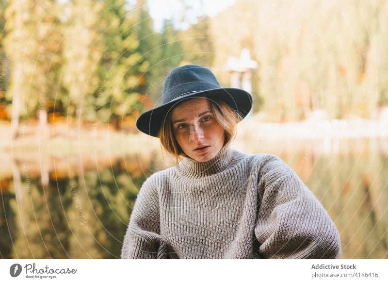 Stylish traveler in hat on shore against lake tourist cool style trip reflection tree woman sky stylish apparel garment confident trendy water mirror beautiful