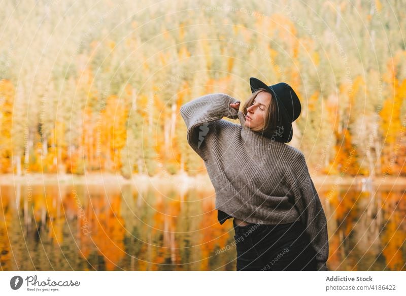 Stylish traveler in hat on shore against lake tourist cool style trip reflection tree woman sky stylish apparel garment confident trendy water mirror beautiful