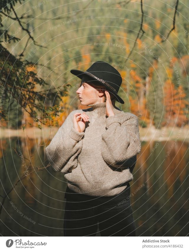 Stylish traveler in hat on shore against lake tourist cool style trip reflection tree woman sky stylish apparel garment confident trendy water mirror beautiful