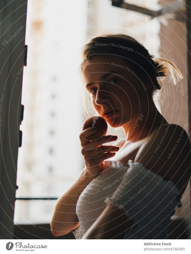 Beautiful woman with peach standing in modern kitchen dreamy snack serene positive peaceful feminine counter tranquil charming bare shoulders attractive