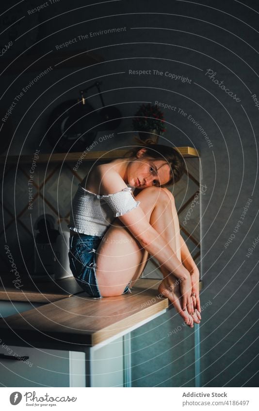 Pretty woman sitting on kitchen counter unemotional calm dreamy casual thoughtful feminine mug tranquil charming bare shoulders attractive beautiful lifestyle