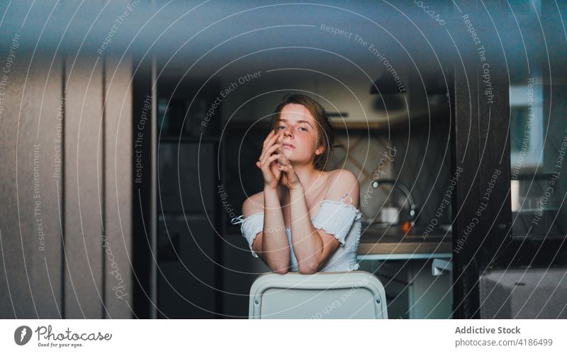 Pretty woman sitting on kitchen counter unemotional calm dreamy casual thoughtful feminine mug tranquil charming bare shoulders attractive beautiful lifestyle