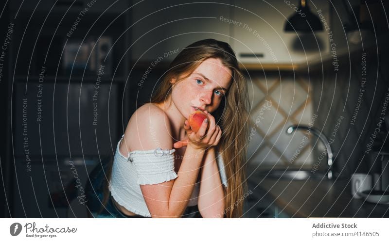 Beautiful woman with peach standing in modern kitchen dreamy snack serene positive lean on peaceful feminine counter tranquil charming bare shoulders attractive