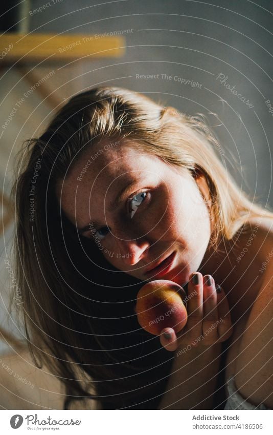 Beautiful woman with peach standing in modern kitchen dreamy snack serene positive lean on peaceful feminine counter tranquil charming bare shoulders attractive