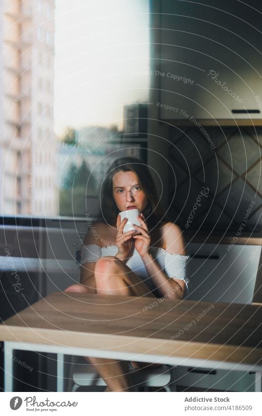 Attractive young woman with cup of hot beverage in kitchen hot drink serene positive counter tranquil charming lean on bare shoulders attractive beautiful