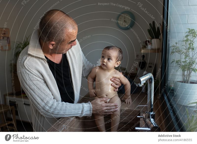 Father washing baby in sink in kitchen bath father adorable toddler naked parent man together parenthood fatherhood dad babyhood bonding home kid love innocent