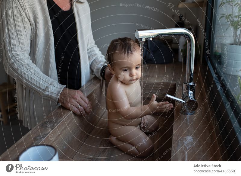 Crop father bathing baby in sink at home wash adorable delight play water kitchen toddler naked parent man together parenthood fatherhood happy cheerful playful