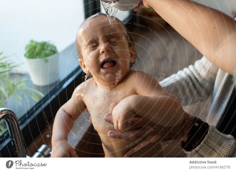 Crop parents bathing baby in kitchen sink water hygiene mother father toddler clean pour cute together child family mom home kid innocent motherhood adorable