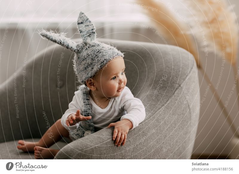 Kid in funny easter bunny costume sits in a chair and laughs baby rabbit suit easter eggs game sitting toy child bed interior sleep newborn boy one leaf smiling