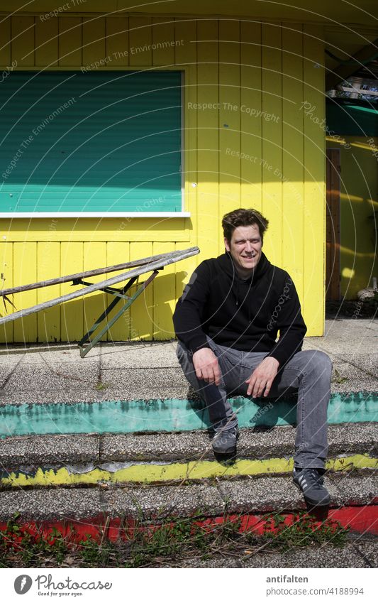 Man sitting casually on the steps in front of a closed kiosk Only one man 1 Person Adults Human being Exterior shot Colour photo Day Stairs stagger Hut Wood