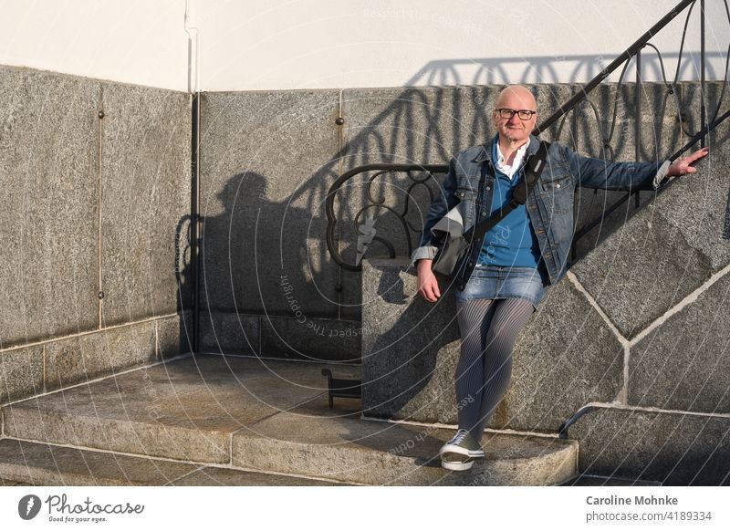 Man in denim jacket, denim mini, houndstooth pattern tights and sneakers at a staircase Fashion Individualist Houndstooth Colour photo Exterior shot Day