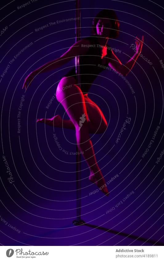 Graceful dancer dancing on pole in neon light touch head legs crossed body eyes closed erotic woman grace arm raised beauty sport bicep art perform sportswoman