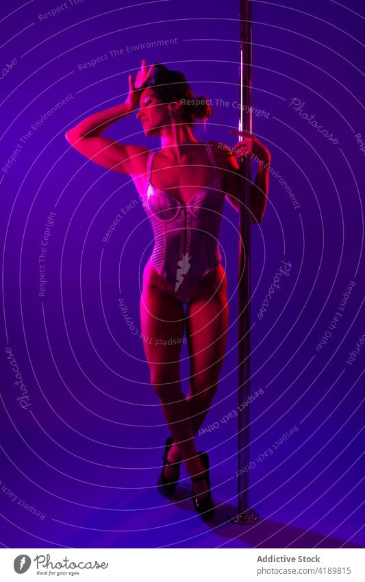 Graceful dancer touching head near dance pole in neon light touch head legs crossed body eyes closed erotic woman grace arm raised beauty sport bicep art