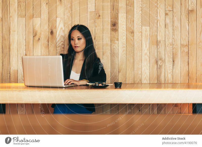 Ethnic businesswoman eating sushi and working on laptop in cafe roll project entrepreneur remote female asian ethnic table busy gadget computer using browsing