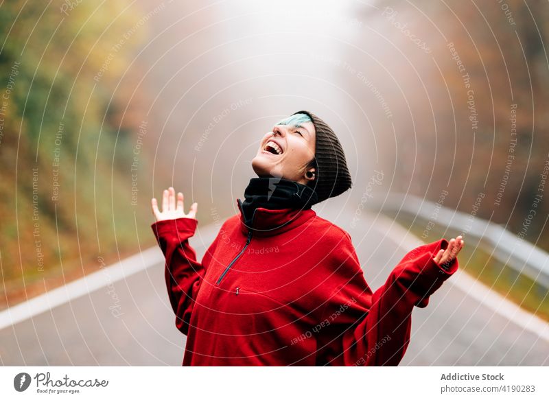 Joyful woman throwing head back on rural road in autumn traveler mist joyful delight happy forest hand raised eyes closed nature enjoy season beautiful positive