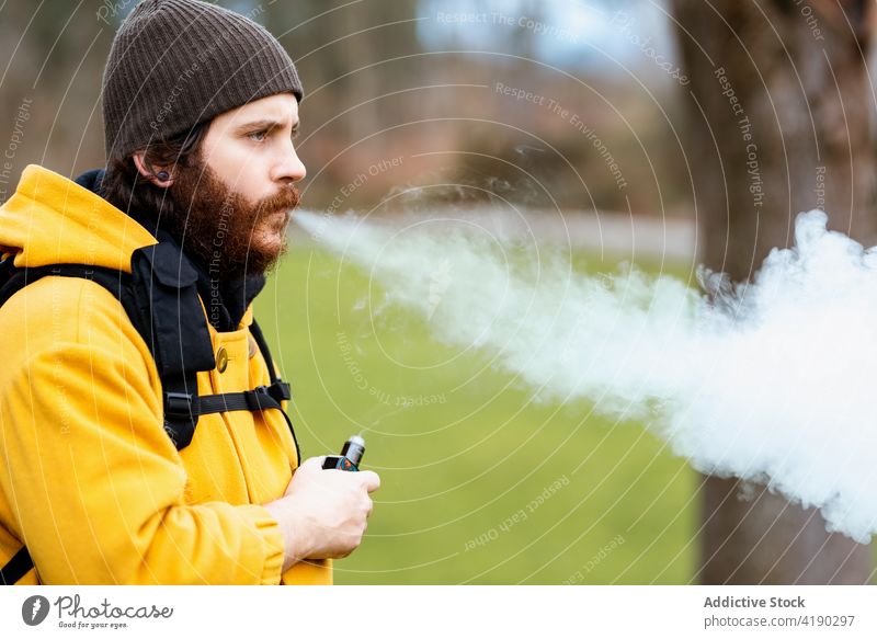 Hipster male tourist vaping on lawn during trip traveler vape exhale hipster brutal steam puff man masculine portrait macho bottle e liquid fog trekker